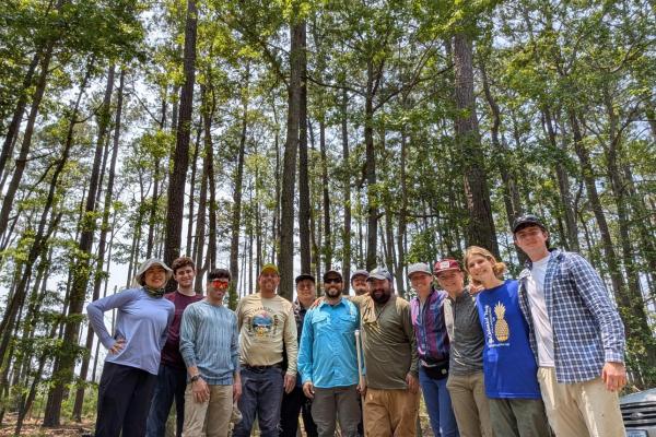 A group of researchers in field gear in a pine forest.